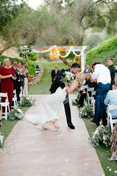 a bride and groom kiss as they walk down the aisle at their outdoor wedding ceremony