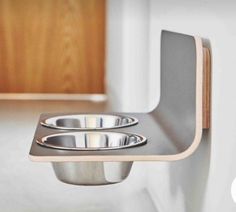 two stainless steel bowls sitting on top of a wooden shelf next to a white wall