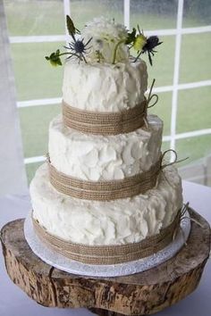 a three tiered wedding cake with flowers on top is sitting on a wooden stand