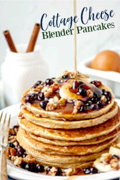 a stack of pancakes topped with blueberries and walnuts on a white plate next to a fork