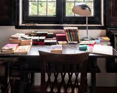 a desk with many books on it and a lamp in front of the window,