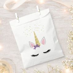 a white paper bag with a unicorn face on it next to some flowers and wine glasses