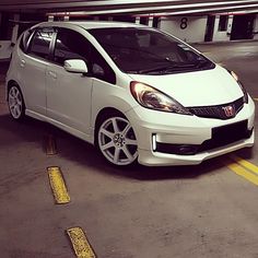 a small white car parked in a parking lot next to a yellow line on the ground