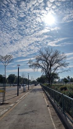 the sun is shining down on an empty street with trees and fenced in area