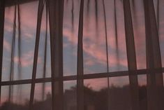 the sun is setting behind sheer curtains in front of a window with trees and clouds