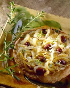 an onion dish with olives and cheese on a wooden platter next to some herbs