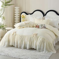 a white bed with ruffled bedspread, pillows and flowers on the headboard