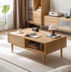 a wooden coffee table sitting in front of a window next to a lamp and book shelf