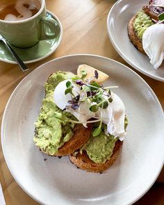 two white plates topped with sandwiches and guacamole next to a cup of coffee