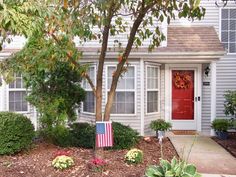 an american flag is in front of a house with red door and green plants on the side