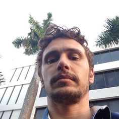 a man standing in front of a tall building with palm trees on the other side