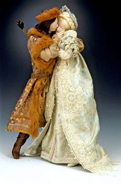 a figurine of two people dressed in period clothing and holding each other's head