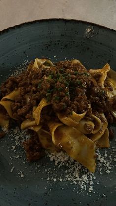 a blue plate topped with pasta and meat covered in sauce on top of a table