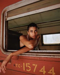 a woman leaning out the window of an old train car with her hand on her hip