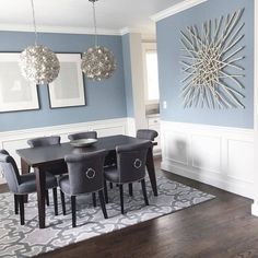 a dining room with blue walls and white wainscothes on the wall, black chairs and a gray rug