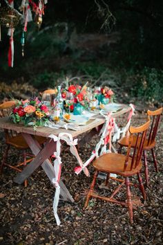 a wooden table topped with lots of flowers and candles next to a forest filled with trees