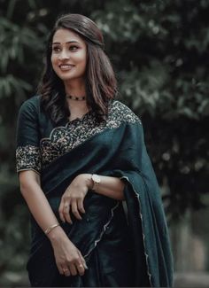 a woman wearing a black sari and smiling at the camera with trees in the background