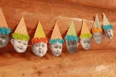 a group of children's hats with faces on them hanging from a line in front of a wooden wall