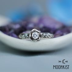 Our beautiful Moissanite Engagement Ring features a faceted 4 mm round gemstone weighing approximately .25 carats. This vintage-inspired mounting is carved to resemble a 3-dimensional rose with delicate detailing.  Roses are a traditional symbol of love and passion that date back hundreds of years. This ring is shown with a laboratory grown D-F Moissanite, but we are happy to create this it for you in a variety of ring sizes, stone choices, and finish options. The Sterling Silver rose that bloom Rose Cut Diamond Flower Promise Ring, Flower Ring With Rose Cut Diamonds For Gifts, Diamond White Flower Ring With Rose Cut Diamonds, Promise Ring With Center Stone, Sterling Silver Flower Ring With Rose Cut Diamonds, Sterling Silver Flower Ring With Round Cut, Flower Engagement, Buy Jewellery Online, Flower Engagement Ring