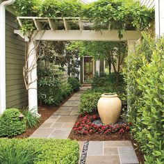 an outdoor garden with lots of greenery and flowers on the side of the house