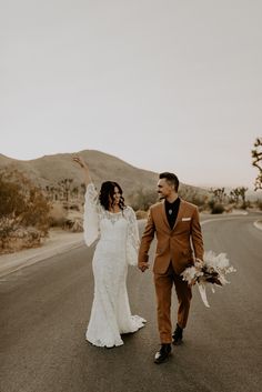 a bride and groom are walking down the road holding their arms in the air as they hold hands