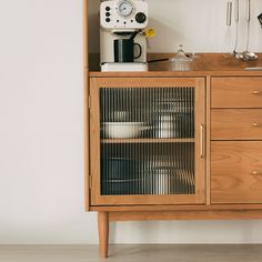 a wooden cabinet with plates and cups on it, next to a coffee maker in the background