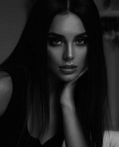 a black and white photo of a woman with her hand on her chin looking at the camera