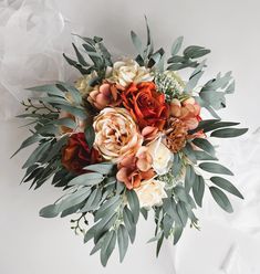 an arrangement of flowers and greenery on a white surface