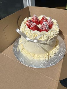 a cake with white frosting and strawberries on top is in a cardboard box