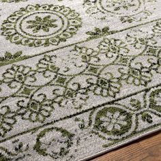 an area rug with green and white designs on the top, sitting on a wooden floor