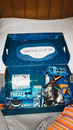 an open blue box on top of a bed filled with snacks and other things to eat