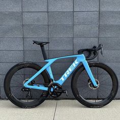 a blue trek bike parked in front of a gray brick wall with black spokes