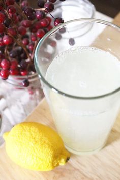 a glass of milk next to a lemon on a cutting board with berries in the background