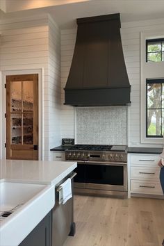 a woman sitting on a counter in a kitchen next to an oven and stove top