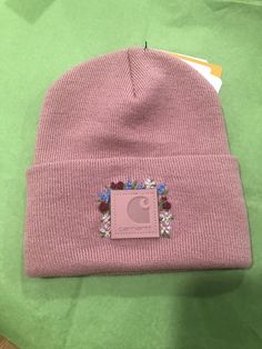 a pink beanie with flowers on it sitting on top of a green tablecloth