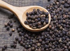 a wooden spoon filled with black pepper on top of a table