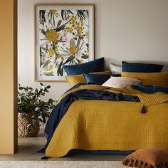 a bedroom with yellow and blue bedding in the corner next to potted plants