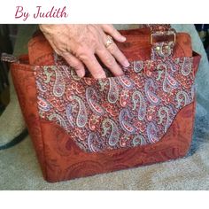 a woman's hand is holding onto an orange and pink paisley purse with gold hardware