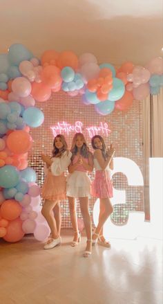 three girls standing in front of a large balloon arch