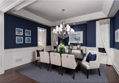 an elegant dining room with blue walls and white chairs, chandelier and pictures on the wall