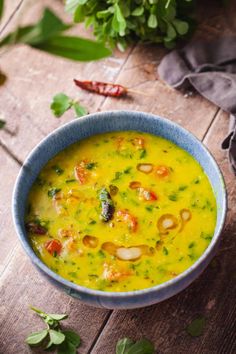 a blue bowl filled with soup sitting on top of a wooden table next to green leaves