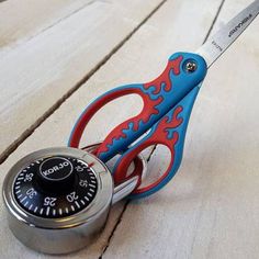 a blue and red pair of scissors sitting on top of a wooden table next to a lock