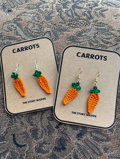 two carrot shaped earrings are on display in front of a lace doily with words carrots the story shoppe