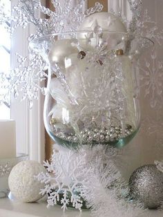 a glass vase filled with white snowflakes and ornaments on top of a mantle