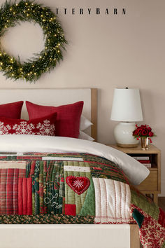 a bed with red and green quilts on it next to a christmas wreath hanging above the headboard