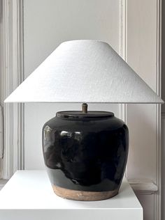 a black vase sitting on top of a white table next to a light fixture with a white shade