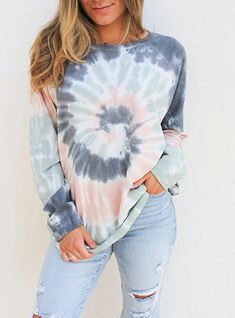 a woman standing in front of a white wall wearing ripped jeans and a tie dye top