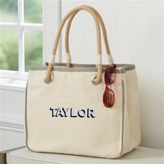 a white tote bag sitting on top of a table next to a window with sunglasses