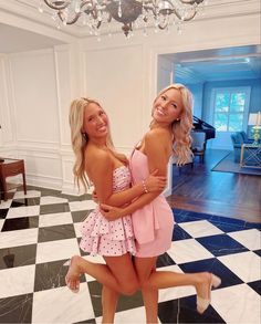 two beautiful young women standing next to each other in front of a chandelier