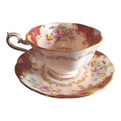 an antique tea cup and saucer with gold trimmings on the rim, decorated with flowers